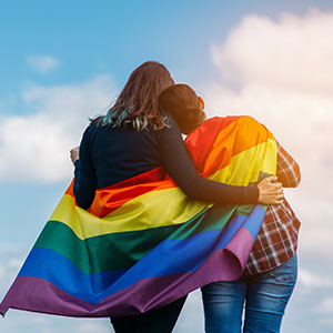Couple wrapped in rainbow pride flag for California discrimination behavior targeting sexual orientation.